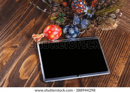 Easter composition. Holiday wreath with colored eggs and tablet pc with blank screen on a wooden table. Easter theme