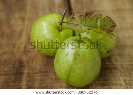 closeup picture of branch with three ripe green guavas on ripped brown wooden table background