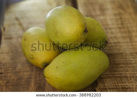 closeup picture of four green ripe mangos on ripped brown wooden table background
