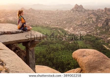 Young woman meditating over ancient city landscape on sunrise in Hampi, India. Copy space Royalty-Free Stock Photo #389002258