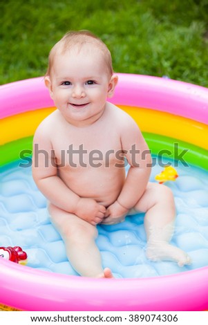 Small chest two teeth smiling child Small chest two teeth smiling child sitting in water in bright multi-colored inflatable pool in the summer on a green grass