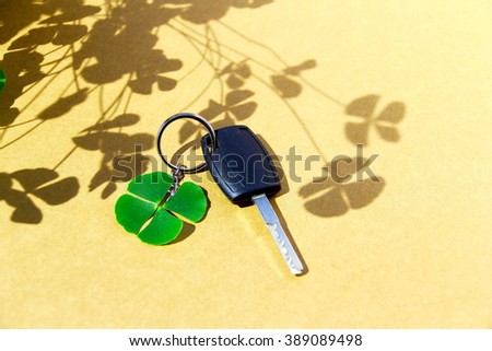 Key car and clover leaf. 4-leaf clover and car key on paperboard background with clover shadow. Conceptual image about lucky.   