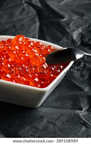 spoon of salmon caviar in a white bowl on a black background vertical format
