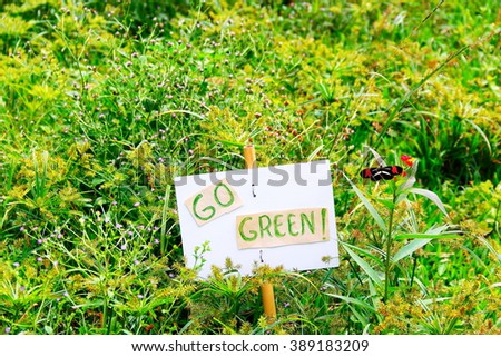 Go green! A small banner that says go green placed on a bamboo stick with a live tropical butterfly sitting on a flower, taken in Southern Brazil    