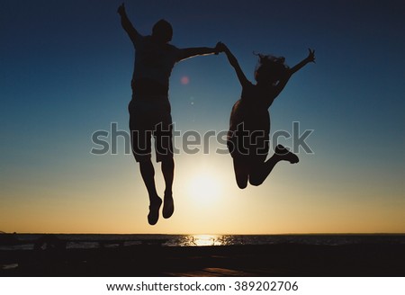 Concept of long-awaited vacation: Young couple in a jump on the sea beach at sunset.