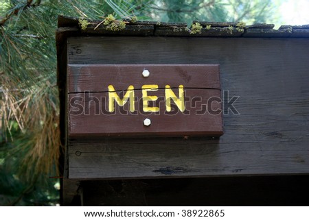 A wooden sign hung over the entrance to a men's room in a woodsy area