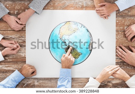 global business, people and team work concept - close up of hands on table pointing finger to earth globe picture in office