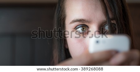 Young woman looking at her cellular phone while using it.  Girl makes contacts in digital world of social networks, connecting people together.  Hands holding phone, partially block lower face. 