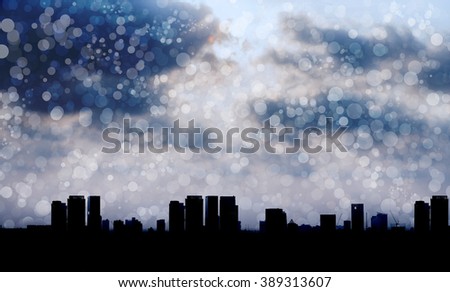 Silhouetted city with light from cloudy sky and light snow blow in the air