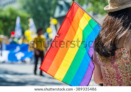 A female spectator is holding the gay rainbow flag at the 2015 Gay Pride Parade in Montreal. Royalty-Free Stock Photo #389335486