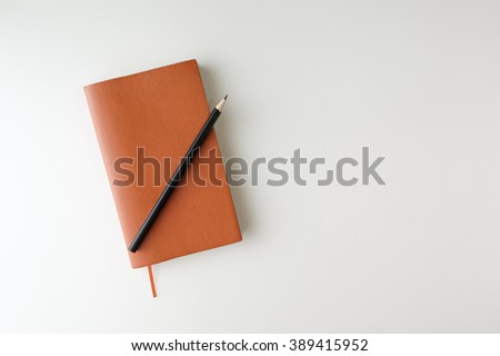 top view blank orange leather diary and pencil on white desk Royalty-Free Stock Photo #389415952
