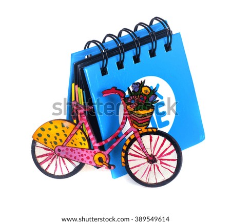 little blue notebook next to which is a small bicycle painted, handmade, white background