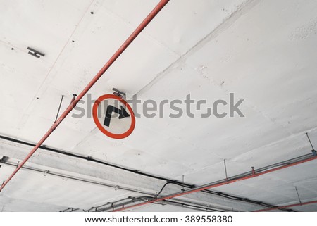 Turn-right sign hanging under the white ceiling of parking lot building.  Red tubes are part of the ceiling. Covered with dust.