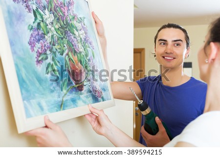 Smiling man and woman hanging art picture in frame