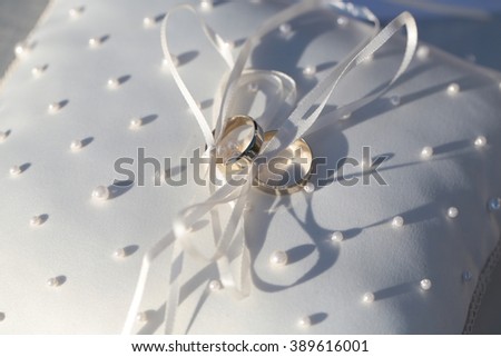 Two golden rings for wedding ceremony jewelry symbol of love on white elegant pillow decorated with beautiful bow and pearl beads closeup, horizontal picture