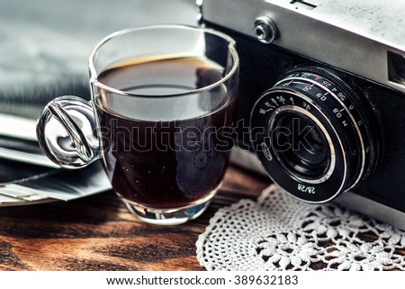 Close up photo of old, vintage camera lens with cap of coffee and black and white photos over wooden table. Nostalgic holidays background. Memories concept. Image is retro filtered. Selective focus