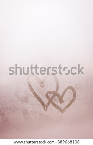 Love heart couple symbol drawn by hand on the wet frozen window glass with sunlight background. Close up