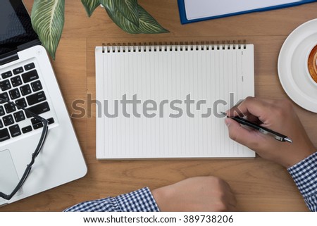 man hand notebook and other office equipment such as computer keyboard, digital tablet, pencil, mug of coffee and glasses on wooden office desk.