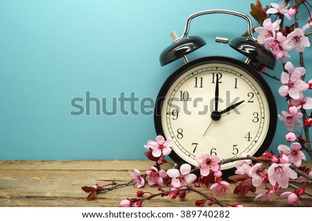 Spring Time Change / Pink Blossoms and an Alarm Clock on an Old Wooden Table Royalty-Free Stock Photo #389740282