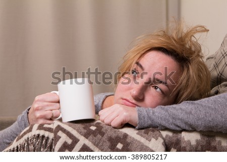 tired or ill girl lie on brown divan and grown plaid and hold white mug