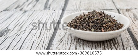 Loose dried darjeeling black tea leaves  in white bowl over wooden background