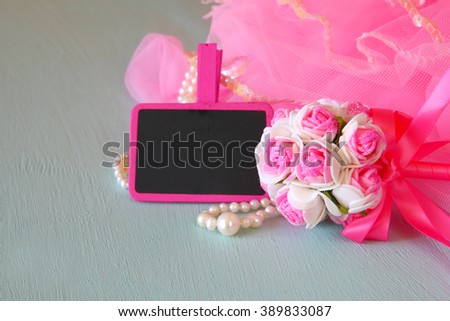 Small girls party outfit: pearls and wand flowers next to small empty chalkboard on wooden table. bridesmaid or fairy costume