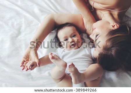 Portrait of beautiful mom playing with her 4 months old baby in bedroom, top view