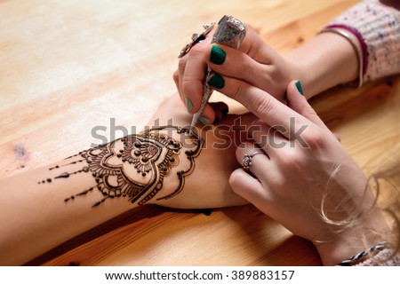 young woman mehendi artist painting henna on the hand Royalty-Free Stock Photo #389883157