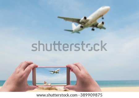 The women shooting image with smart phone on blue sea and white sand beach with plane and some people blurred background