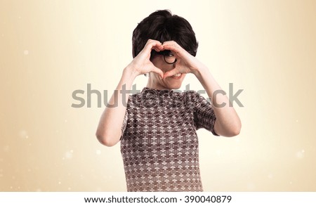 Girl making a heart with her hands over ocher background