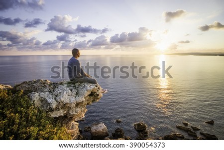 Man Watching Sunrise Sitting On Rock Next To Cliff. Malta, Europe Royalty-Free Stock Photo #390054373