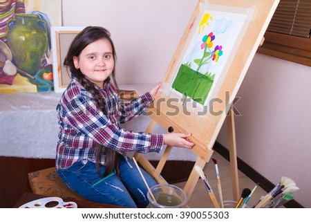 Girl with a painted picture sits beside the easel