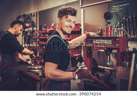 Professional car mechanic working with hydraulic press in auto repair service. Royalty-Free Stock Photo #390074254