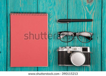 Red Notepad, camera, glasses and pen on the wooden desk