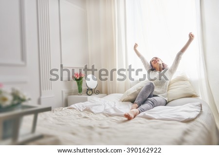 Happy young woman enjoying sunny morning on the bed  Royalty-Free Stock Photo #390162922