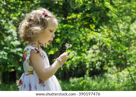 Cute little girl blowing on a dandelion. Selective focus.