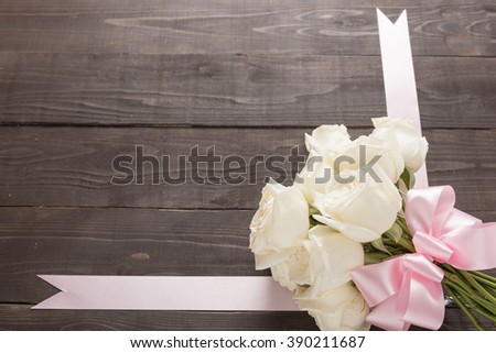 White roses flower with ribbon are on the wooden background.