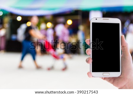Girl use mobile phone, blur image of mother and baby shopping at street market as background.