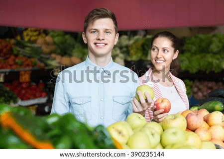 Happy young husband helping girl to choose veggies and fruits . Focus on man
