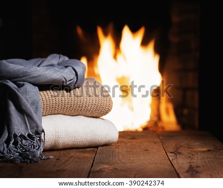 Warm woolen things near fireplace on wooden table. Winter and Christmas holiday concept.
