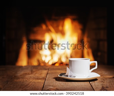 White cup of tea with teabag on wooden table near  fireplace. Winter and Christmas holiday concept Royalty-Free Stock Photo #390242518