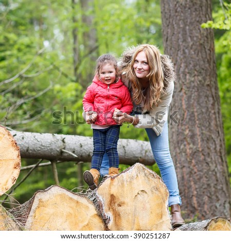 Mother and cute kid girl outdoors playing, kissing and hugging. Happy family of two, young smiling woman and her cute toddler daughter enjoying beautiful day in the forest