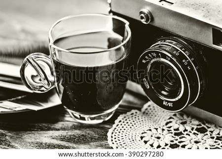 Close up photo of old, vintage camera lens with cap of coffee and black and white photos over wooden table. Nostalgic holidays background. Memories concept. BW image. Selective focus