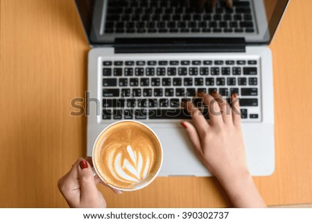 Laptop and coffee cup in girl's hands sitting on a wooden background