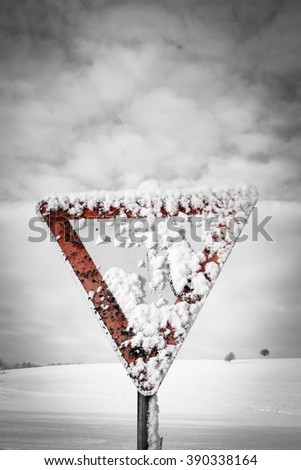 give way traffic sign, traffic sign, yield sign, with blue sky and clouds and with snow in winter season