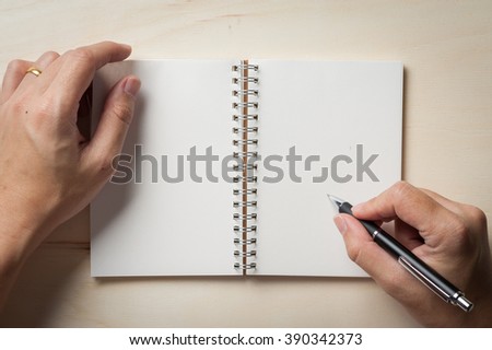 Male right hand writing on opened notebook with blank area for text or message and pen on wood table in morning time