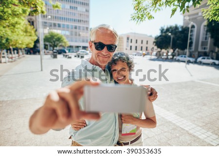 Loving senior couple embracing and taking a selfie on mobile phone outdoors. Tourist taking self portrait during a foreign city vacation.