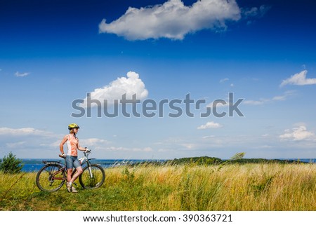 Happy girl with bicycle looking at  view in a green meadow
