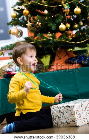Happy little boy opening Chrismas present at Christmas Eve under the Christmas tree.