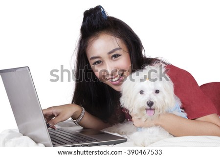 Picture of pretty model smiling at the camera while using laptop computer with her dog on bed